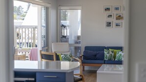 A modern living room with a sofa, a dining area with a table and chairs, and a kitchen area with a microwave. - Family Oasis - Pauanui Holiday Home (Pauanui)