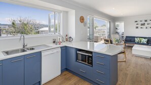 A modern kitchen with a dishwasher, microwave, and a large window. - Family Oasis - Pauanui Holiday Home (Pauanui)