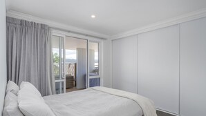 A bedroom with a bed, curtains, a sliding door to a balcony, and a white wardrobe. - Family Oasis - Pauanui Holiday Home (Pauanui)