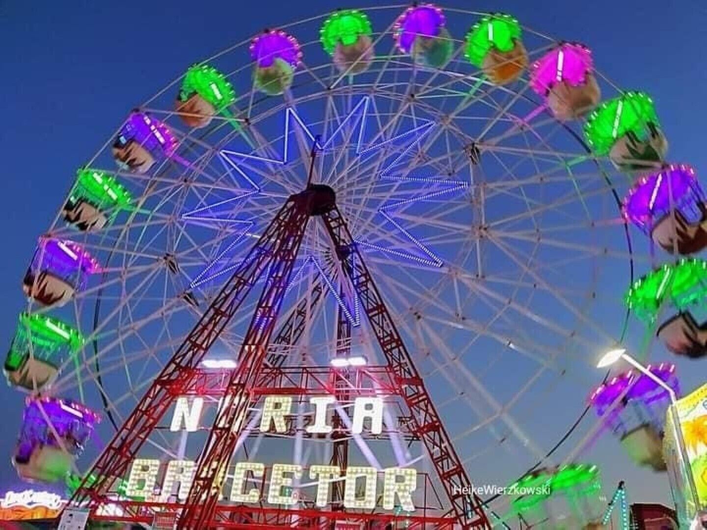 A Ferris wheel with colorful lights and the words "NATURA DIRECTOR" visible on its structure.