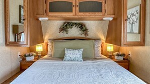 Un dormitorio con una cama grande, armarios de madera arriba y dos mesitas de noche con lámparas y jarrones de flores.