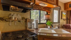 Una cocina compacta con estufa a gas, cafetera y lavamanos.