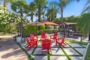 A patio with red chairs, a pergola with white flowers, and palm trees. - Erwin Estate (Woodland Hills)