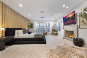 A modern bedroom with a large bed, a fireplace, and a large painting on the wall. - Erwin Estate (Woodland Hills)