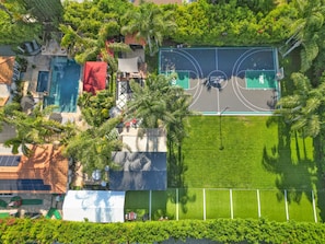 Vista aérea de uma propriedade com piscina, quadra de tênis e vegetação exuberante.