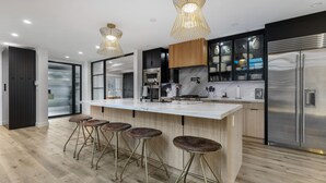 A modern kitchen with a large island, bar stools, stainless steel appliances, and pendant lighting. - Erwin Estate (Woodland Hills)