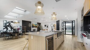A modern kitchen with a central island, pendant lighting, and a dining area with a black and white abstract painting. - Erwin Estate (Woodland Hills)