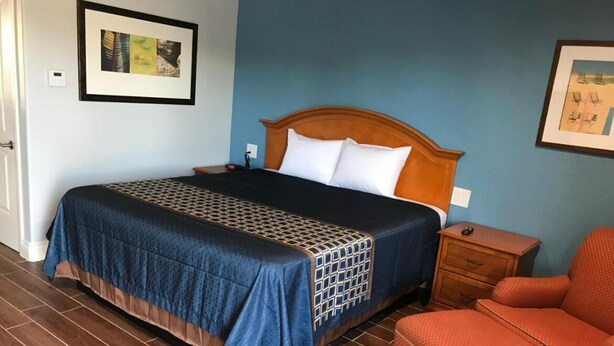 Habitación de hotel con una cama grande, cabecera de madera, mesita de noche, sillón rojo y piso de baldosas.