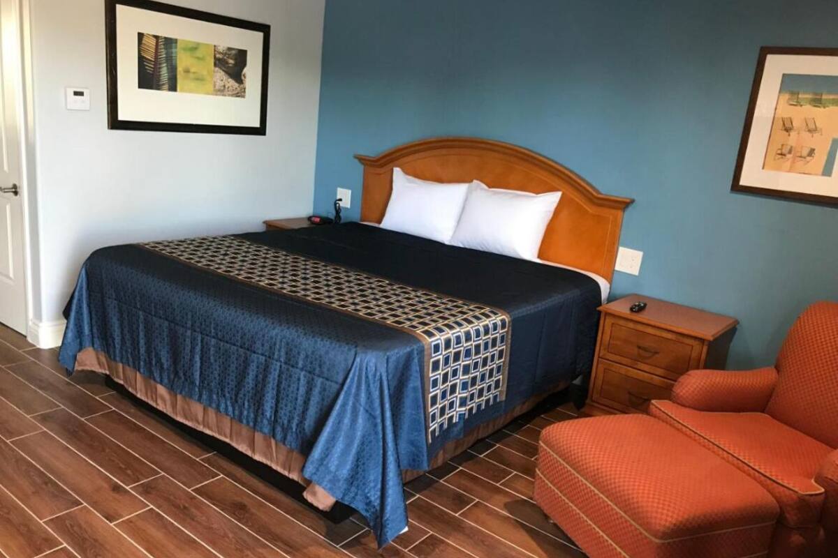 Een hotelkamer met een groot bed, een houten hoofdeinde, een nachtkastje, een rode fauteuil en een betegelde vloer.