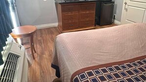 Un dormitorio con cama, cómoda, televisor y calefactor.