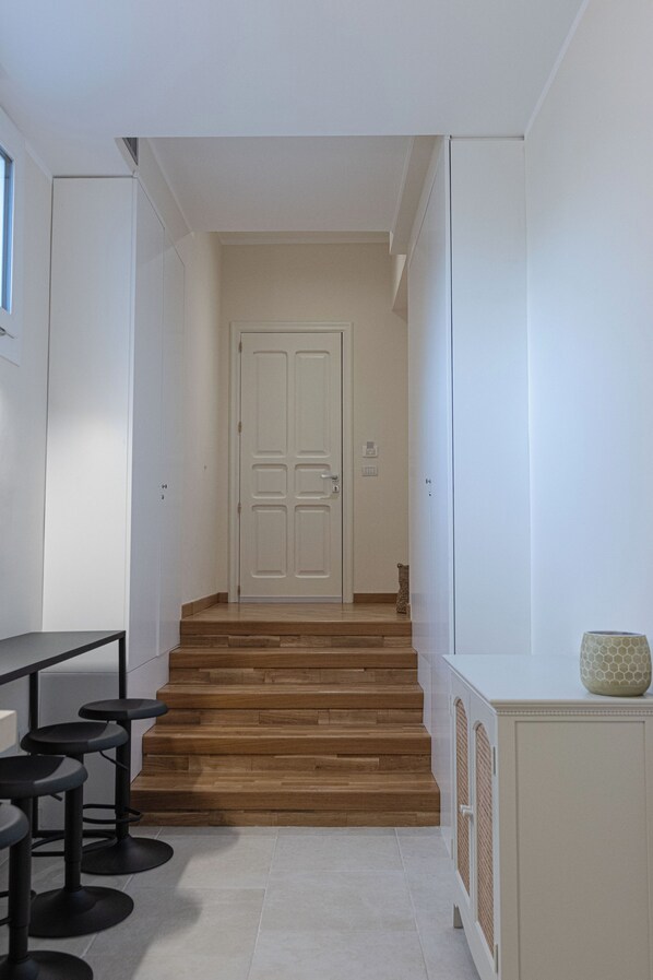 A hallway with a staircase leading to a door, a bar area with stools, and a cabinet with a decorative item on top.