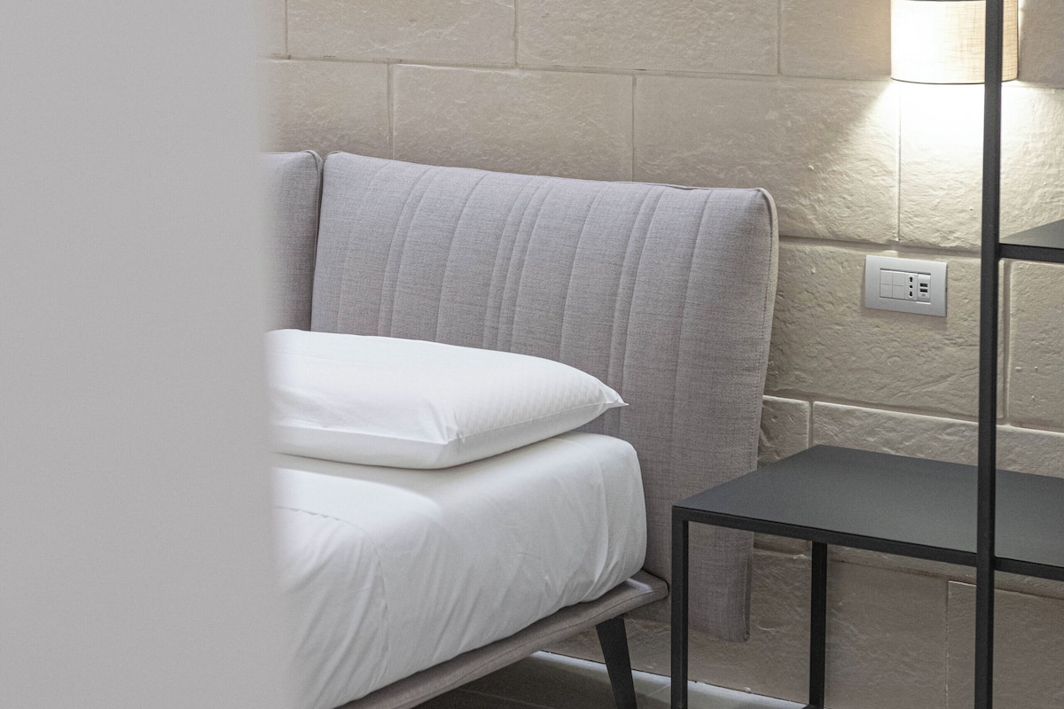 A bedroom with a bed, a bedside table, and a wall-mounted lamp.