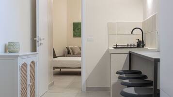 A modern kitchen with a black faucet, a small island with stools, and a door leading to a bedroom with a bed and pillows.