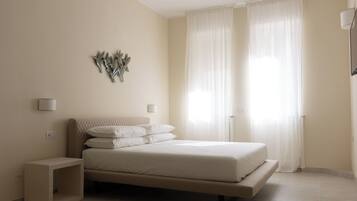 Une chambre à coucher avec un lit, des tables de chevet, une lampe fixée au mur et des rideaux légers.
