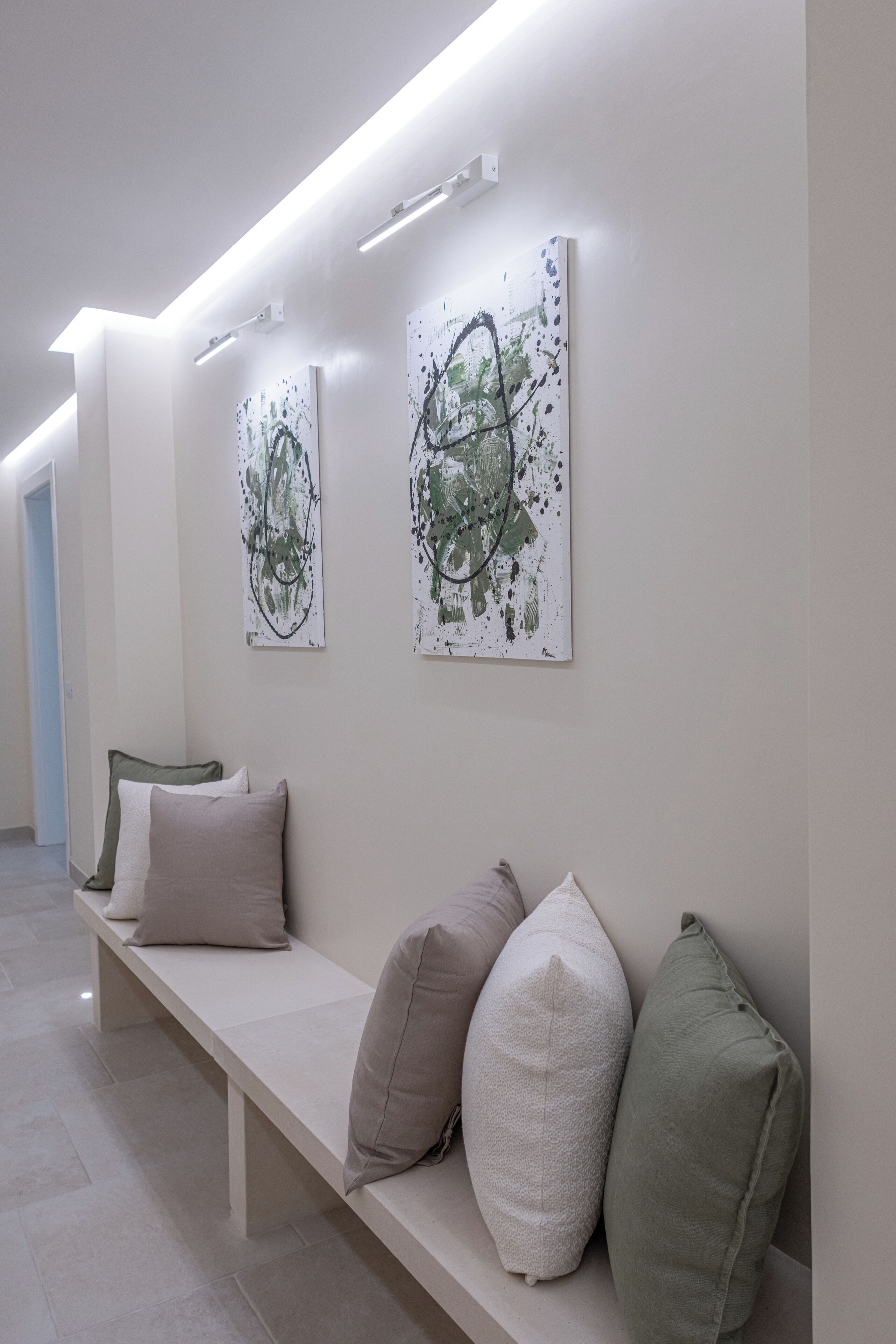 A hallway with a bench, three pillows, and two abstract paintings on the wall.