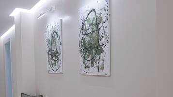 A hallway with a bench, three pillows, and two abstract paintings on the wall.