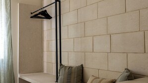 Una habitación moderna con una pared de ladrillo color beige, un banco con cojines, una percha colgante y un mueble pequeño.