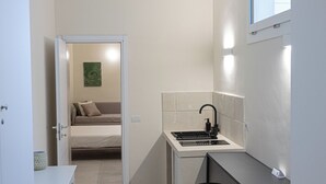 Cocina compacta con estufa integrada, lavamanos y ventana sobre la encimera. Hay tres taburetes y un mueble pequeño.