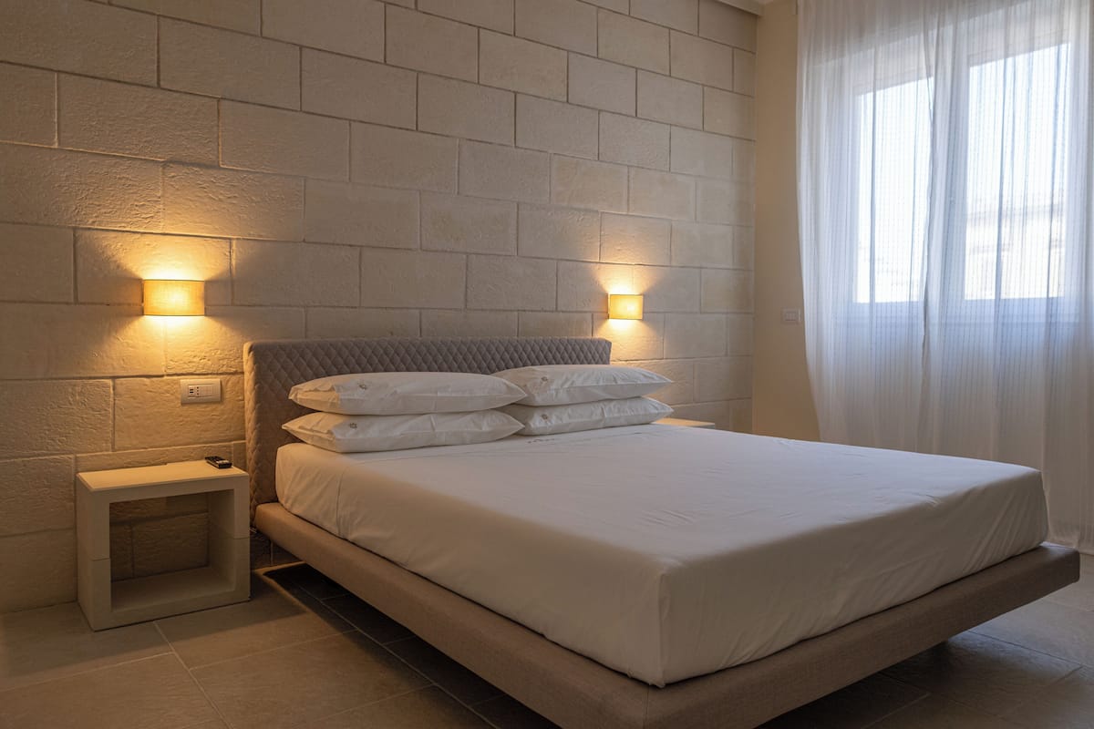 A neatly made bed with white bedding, two bedside lamps, and a small bedside table.