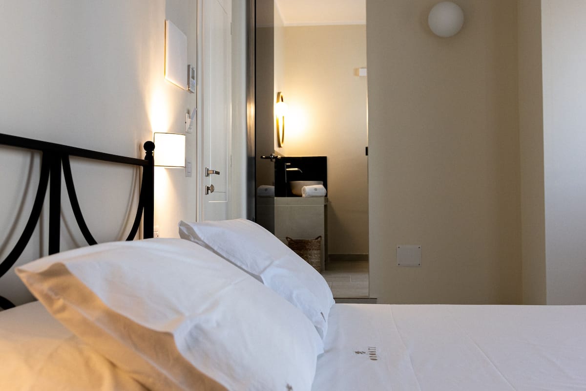 A hotel room with a bed, a nightstand, a mirror, and a bathroom visible in the background.