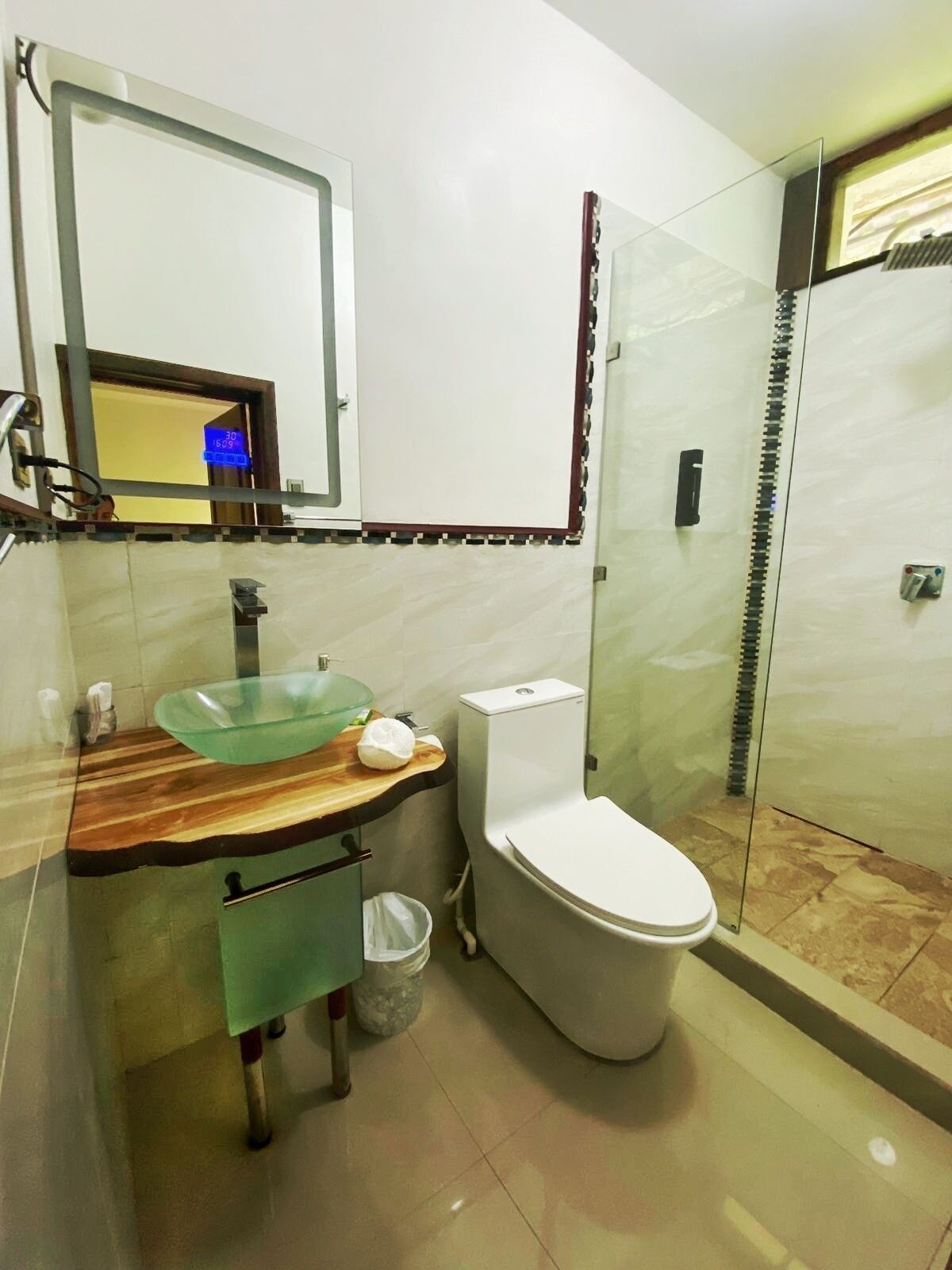 A modern bathroom with a glass sink, white toilet, and a glass shower enclosure.
