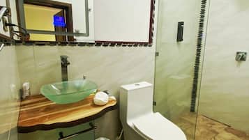 A modern bathroom with a glass sink, white toilet, and a glass shower enclosure.