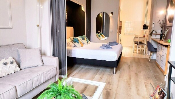 A modern living room with a sofa, a bed with a large mirror, and a dining area with a chair and table. - Kosykasa Spa (Cannes)