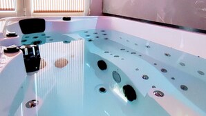 A spa room with a large bathtub, a window with blinds, and two small wall-mounted pictures. - Kosykasa Spa (Cannes)