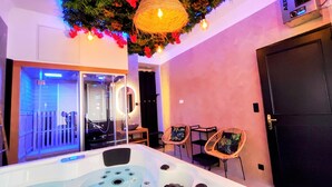 A modern bathroom with a jacuzzi, two wicker chairs, and a decorative ceiling light. - Kosykasa Spa (Cannes)