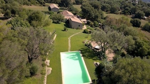 A residential area with a swimming pool, stone houses, and surrounding greenery.