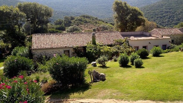 A rural property with stone buildings, a well-maintained garden, and a view of rolling hills in the background.