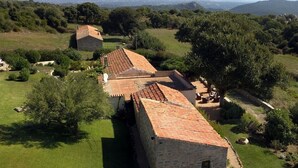A stone building with a tiled roof, surrounded by lush greenery and trees.