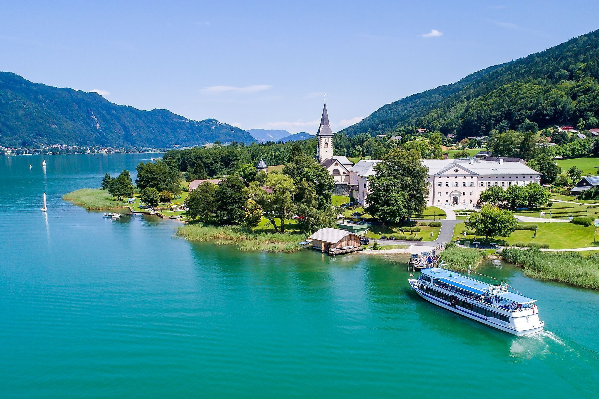 A lakeside town with a church, a large building, and a boat docked near the shore.