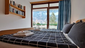 Ein Hotelzimmer mit zwei Betten, einem Bücherregal und einem großen Fenster mit Blick auf die Berge.