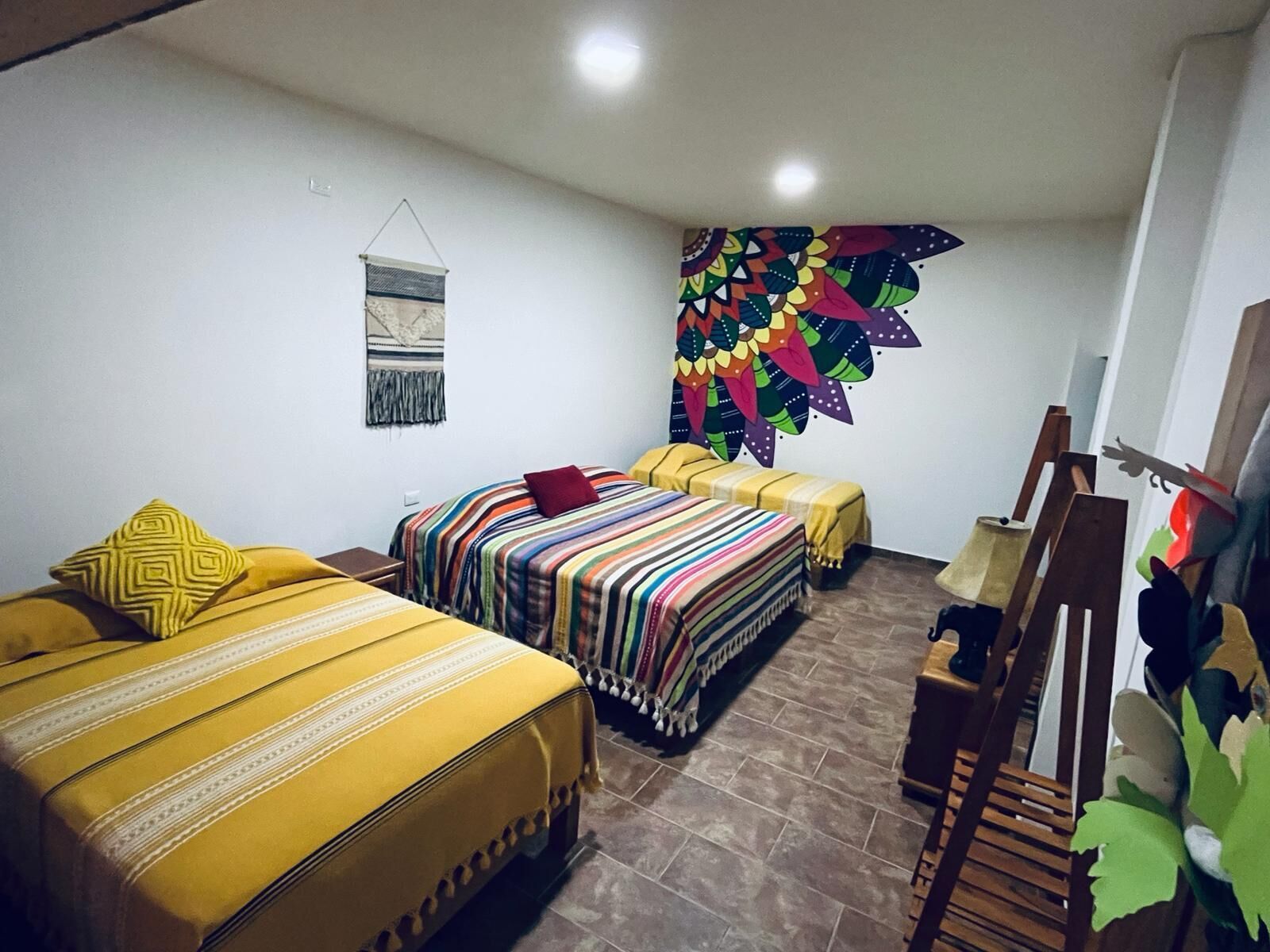 A hotel room with two beds, a wooden bench, a wall tapestry, and a small table.