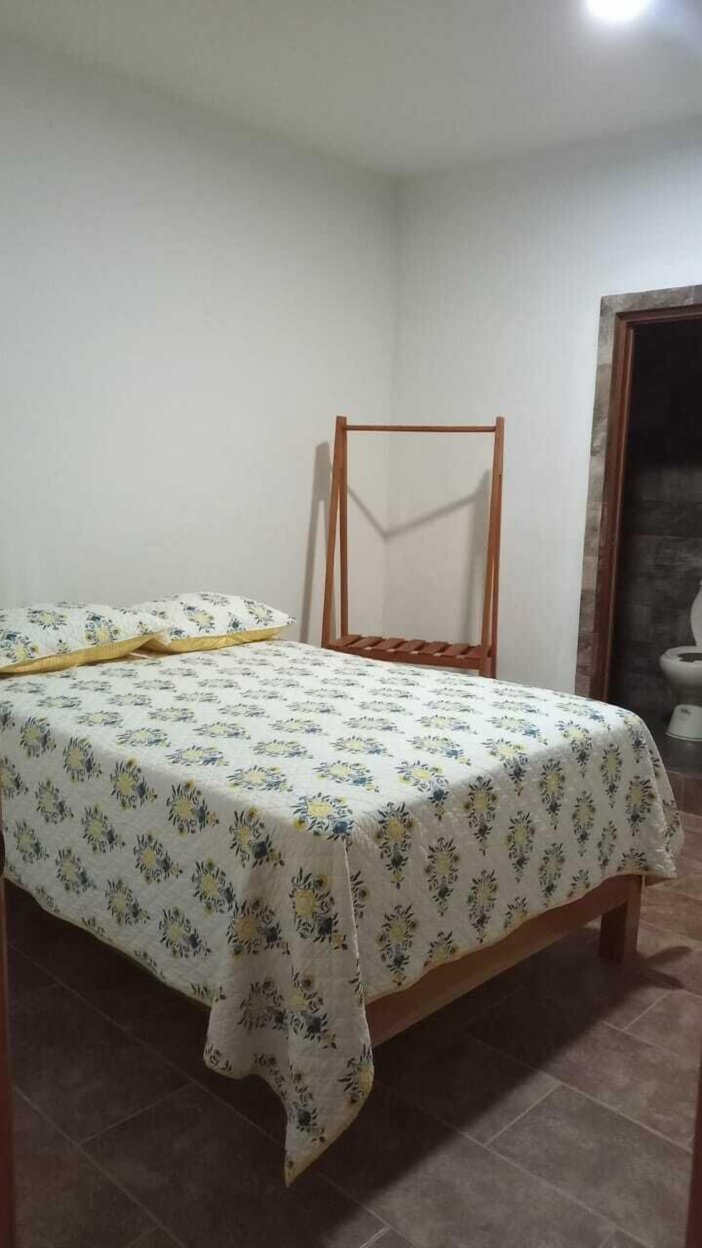 A bedroom with a bed, a wooden chair, and a toilet visible in the corner.