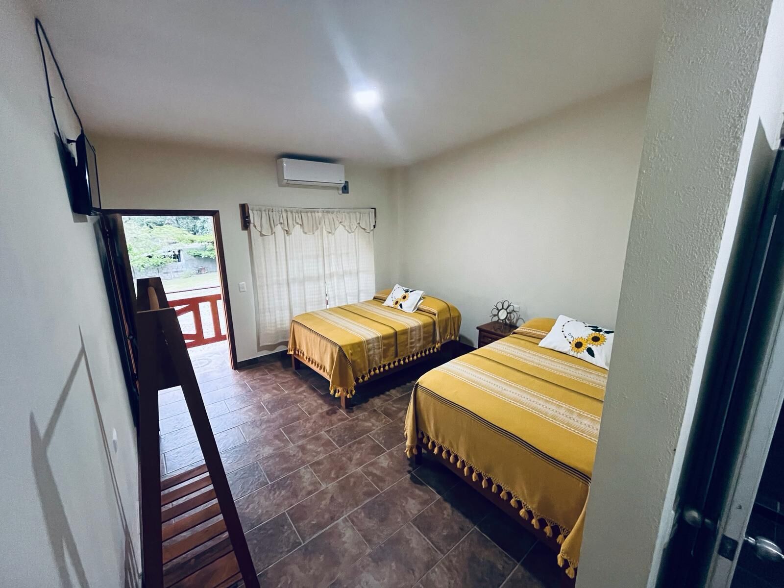 Habitación de hotel con dos camas, una silla de madera, una mesita y una ventana con cortinas.