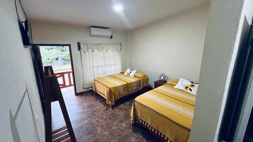 Habitación de hotel con dos camas, una silla de madera, una mesita y una ventana con cortinas.