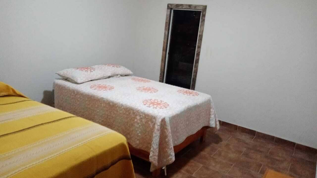 Una habitación pequeña con una cama individual, una pared blanca lisa y piso de baldosas.