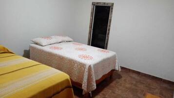 Una habitación pequeña con una cama individual, una pared blanca lisa y piso de baldosas.
