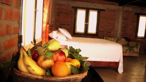 Een kamer met een bakstenen muur, een bed en een mand met fruit op een tafel.