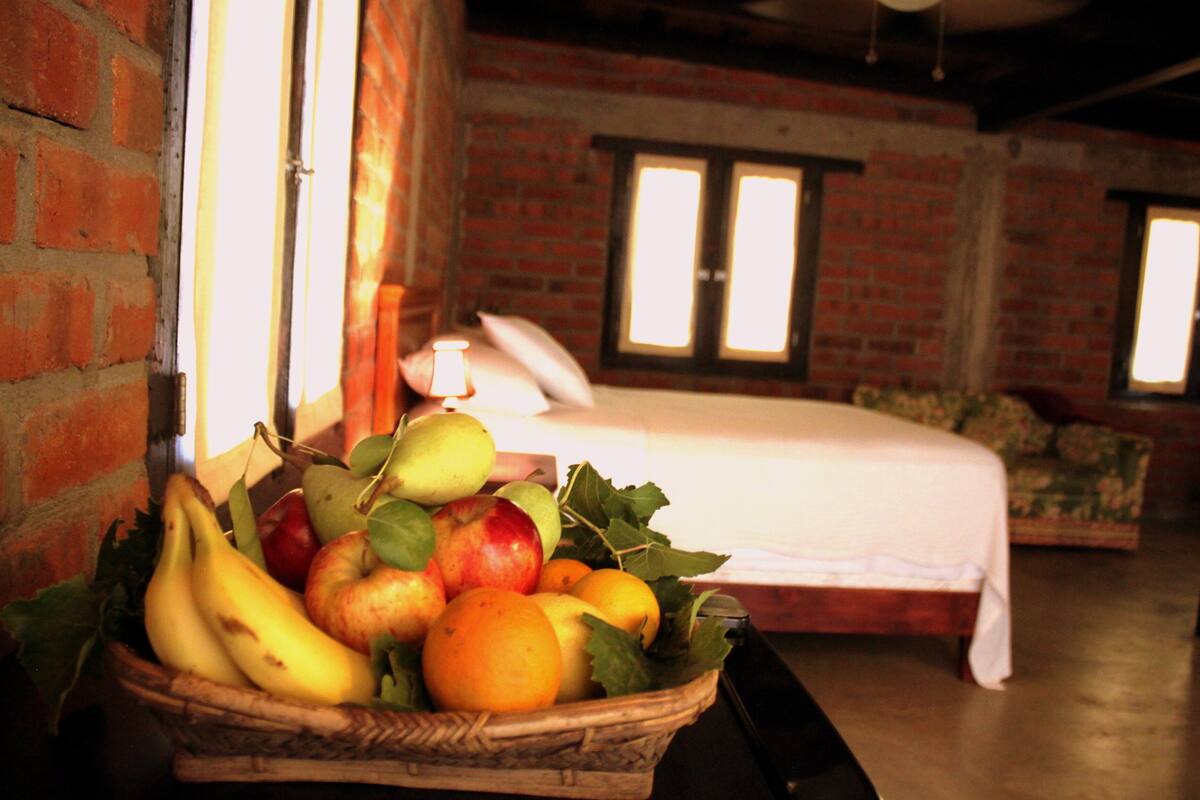 Una habitación con pared de ladrillo, una cama y una cesta de fruta sobre una mesa.
