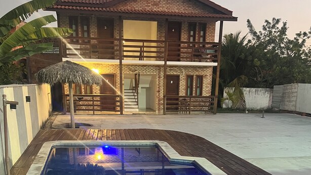 A swimming pool with a wooden deck, a brick house with a balcony, and a thatched roof structure. - Pousada Terra das Águas Barreirinhas (Barreirinhas)