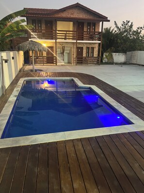 A swimming pool with a wooden deck, a brick house with a balcony, and a thatched roof structure. - Pousada Terra das Águas Barreirinhas (Barreirinhas)