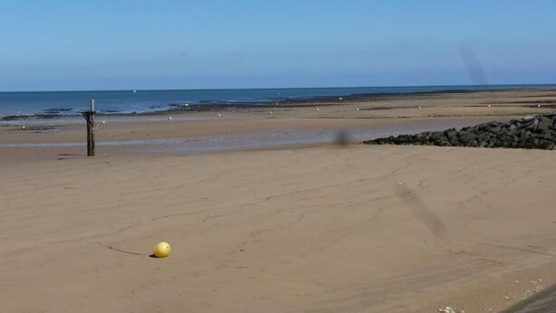 Ein Strand mit einem gelben Ball, einem Holzpfosten und felsigem Gelände.