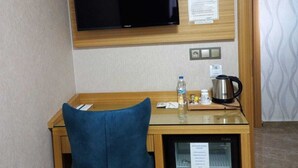 Ett hotellrum med ett skrivbord i trä, en blå stol, en platt-TV, ett minikylskåp, en vattenkokare och en vattenflaska.