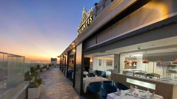 A rooftop restaurant with tables and chairs, a glass railing, and a view of the sunset. - Hotel Atlantis Alger (Algiers)