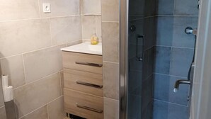 A bathroom with a toilet, a sink with a mirror, and a shower area with a glass door. - Joli T1 au Calme, Entre Collines et Littoral; Idéal Pour Explorer la Région! (Gémenos)