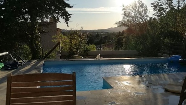 A swimming pool with a wooden chair in the foreground, surrounded by trees and a distant view of mountains. - Joli T1 au Calme, Entre Collines et Littoral; Idéal Pour Explorer la Région! (Gémenos)