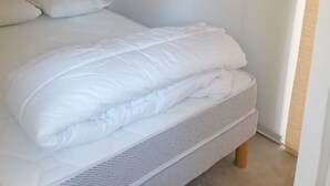 A bedroom with a neatly made bed, a small black object on the wall, and a window on the right. - Joli T1 au Calme, Entre Collines et Littoral; Idéal Pour Explorer la Région! (Gémenos)